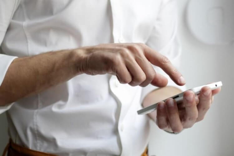 White business shirt with hands holding cell phone while touching screen with one finger.